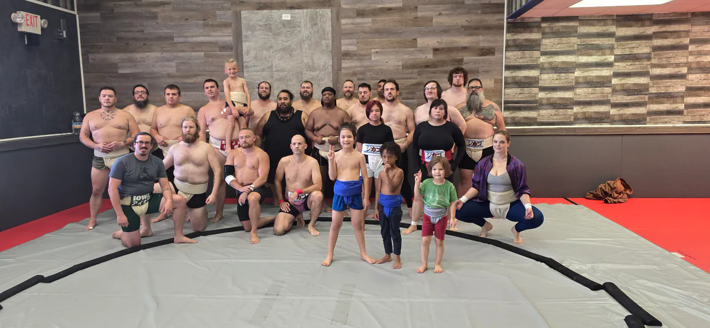 A large group of wrestlers and children posing together on the dohyo